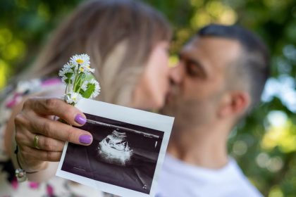 Expecting couple holding ultrasound image, celebrating pregnancy outdoors with a kiss.